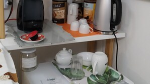 A kitchenette with a microwave, coffee maker, and kettle on a shelf, along with a coffee can and cups on the counter. - AdagioRooms (Elmas)
