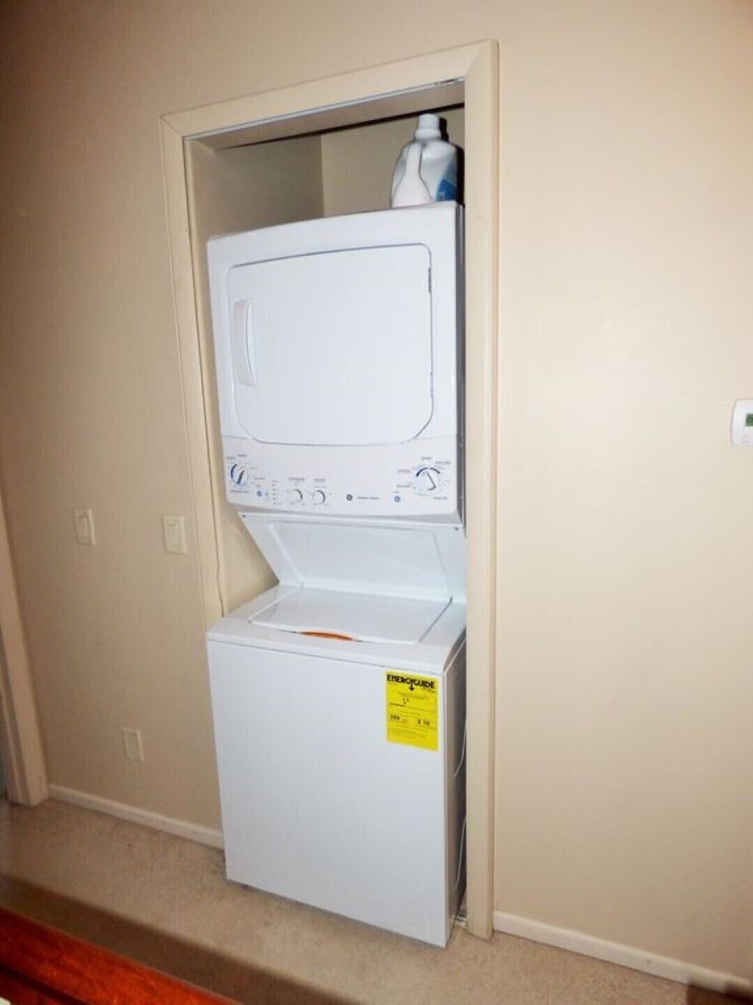 A compact washer and dryer unit in a small laundry room with beige walls and a wooden floor.
