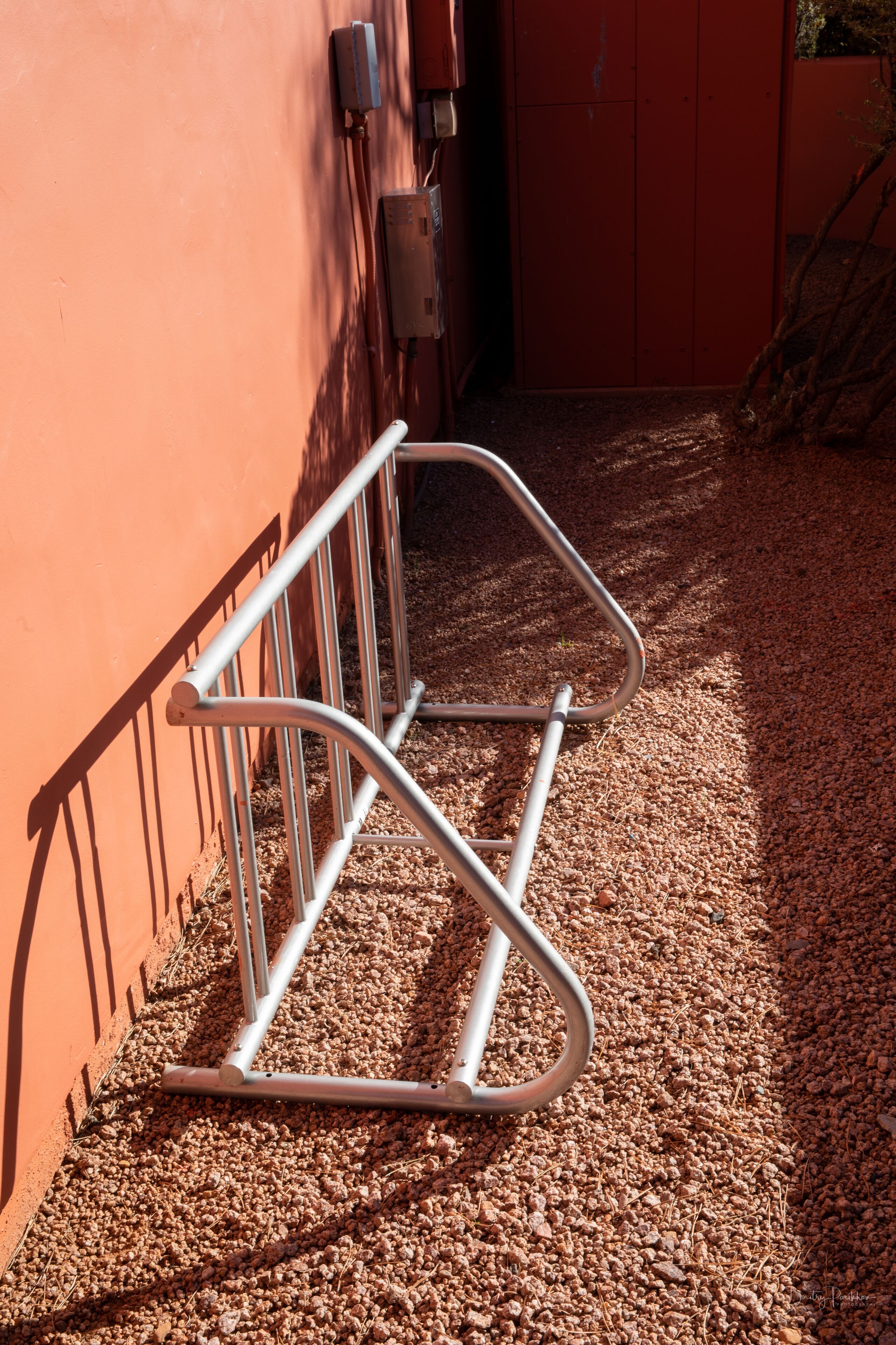 Un support à vélos en métal adossé à un mur, avec un sol recouvert de gravier.