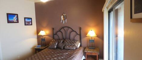 A bedroom with a bed, two bedside tables with lamps, a ceiling fan, and a wall-mounted shelf with a decorative item.