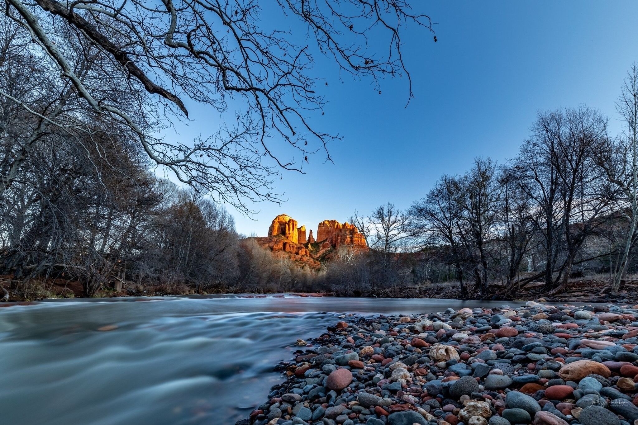 A river with a rocky shore and a prominent rock formation in the background.