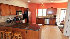 A kitchen with wooden cabinets, stainless steel appliances, a large island with stools, and a bright orange wall.