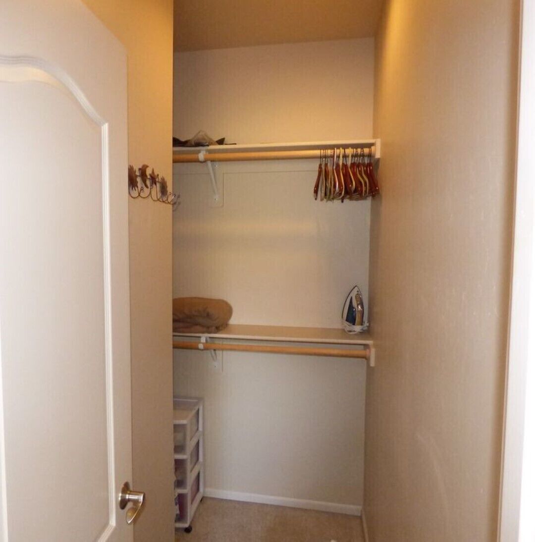 A small walk-in closet with a hanging rod, shelves, and a storage unit.