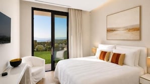 Et moderne hotelværelse med en stor seng, et skrivebord, en stol, et fjernsyn og en skydedør, der fører ud til en balkon med udsigt.