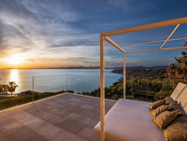 A balcony with a view of the sea and distant mountains at sunset.