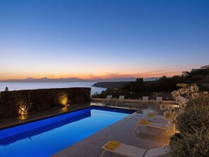 Une piscine avec des chaises longues et une vue sur l’océan au crépuscule.
