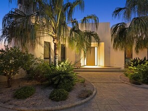 Un bâtiment moderne doté d’une entrée pavée, de palmiers et d’un jardin bien entretenu.
