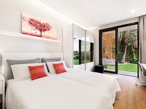 Une chambre moderne avec un grand lit, un tableau représentant un arbre et une porte-fenêtre coulissante donnant sur un jardin.