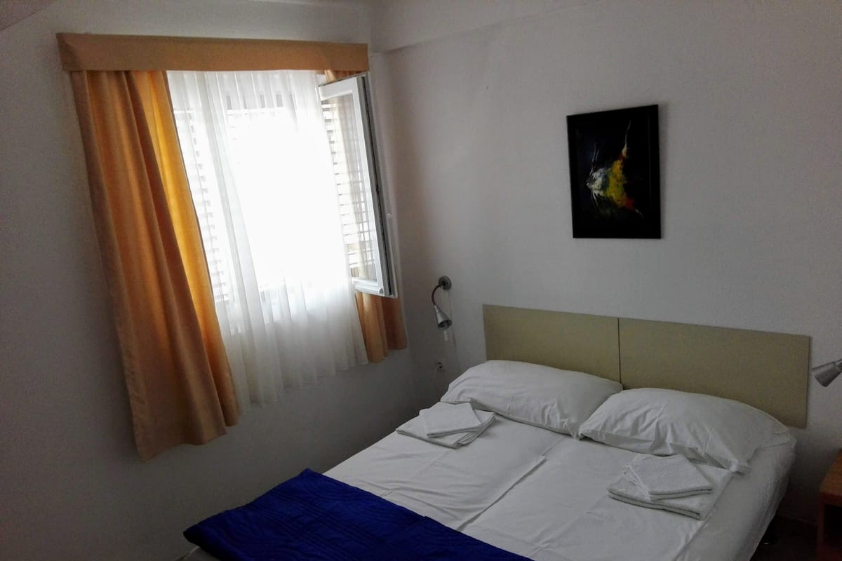 Ein Schlafzimmer mit Bett, einem Fenster mit Vorhängen, einer Wandleuchte und einem Bild.