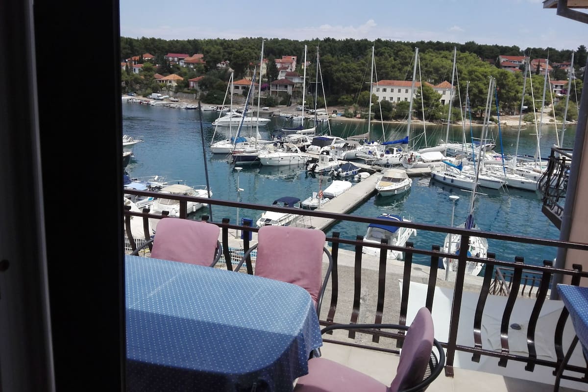 Ein Balkon mit Tisch und Stühlen mit Blick auf einen Hafen voller Boote.