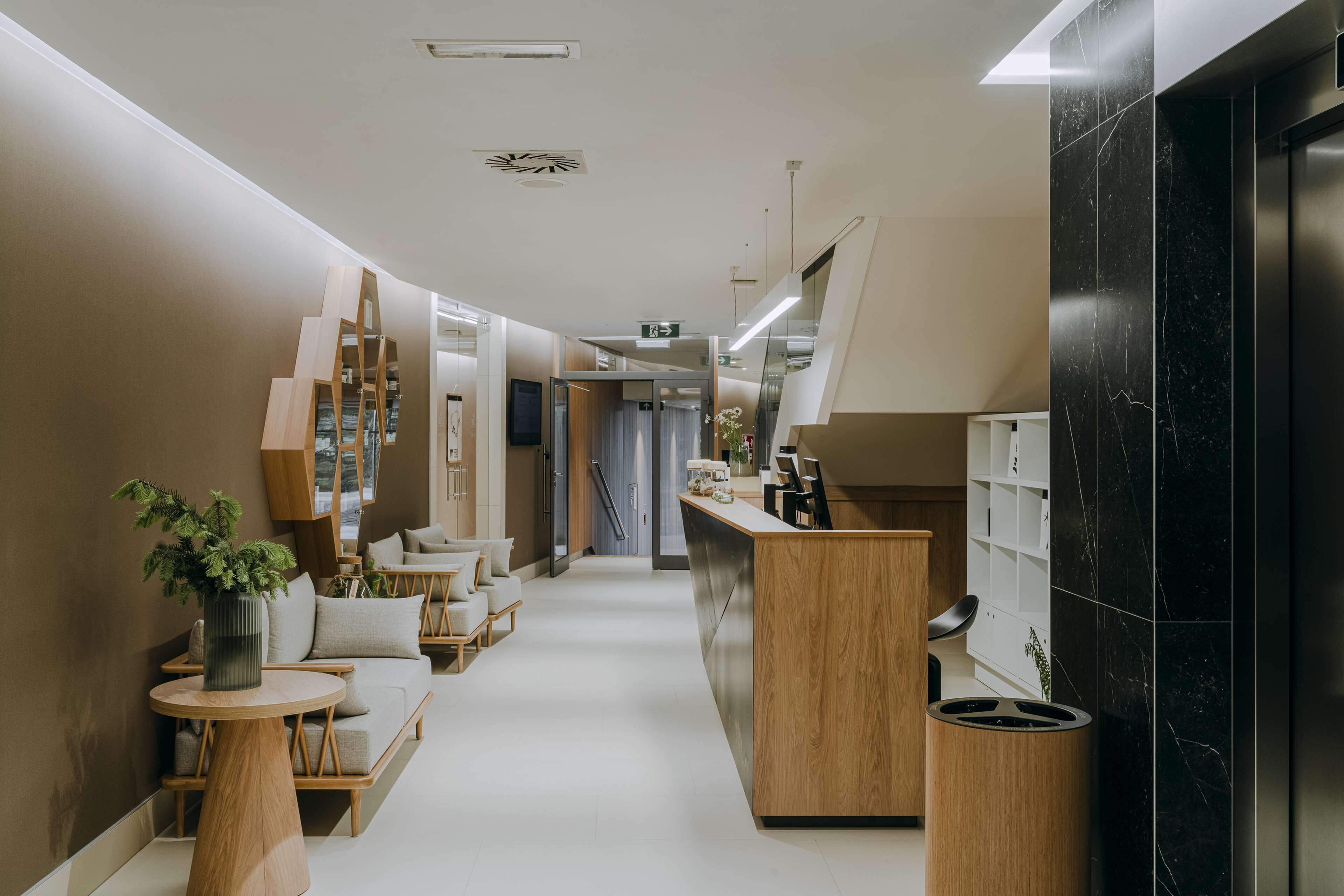 A modern hotel corridor with a reception desk, seating area, and a staircase.