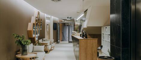 A modern hotel corridor with a reception desk, seating area, and a staircase.
