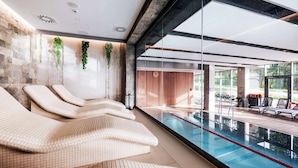 A modern indoor pool area with lounge chairs and a glass wall offering a view of the outside. - Radisson Hotel Szklarska Poręba (Szklarska Poreba)