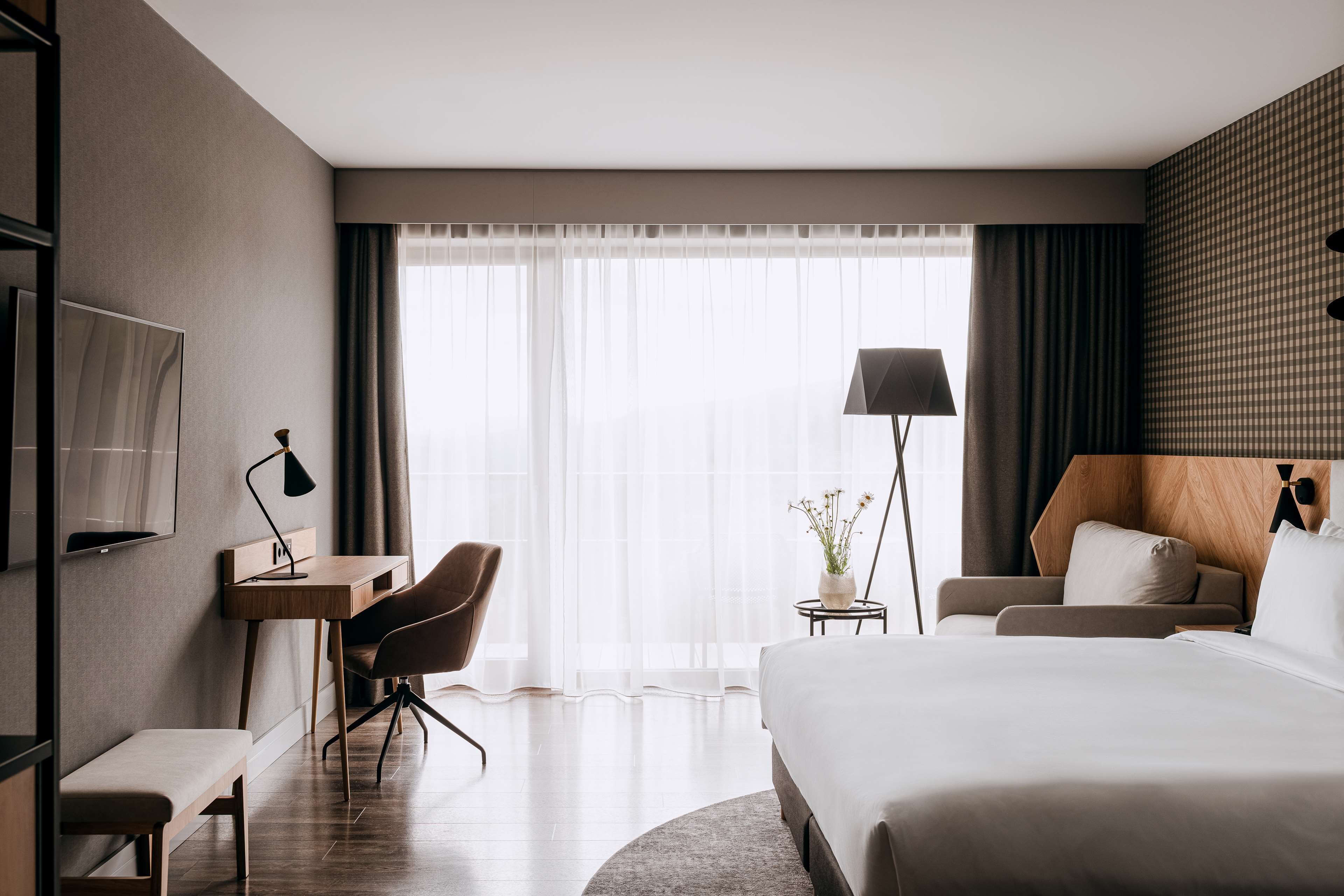 A hotel room with a large bed, a desk with a chair, a TV, and a lamp.