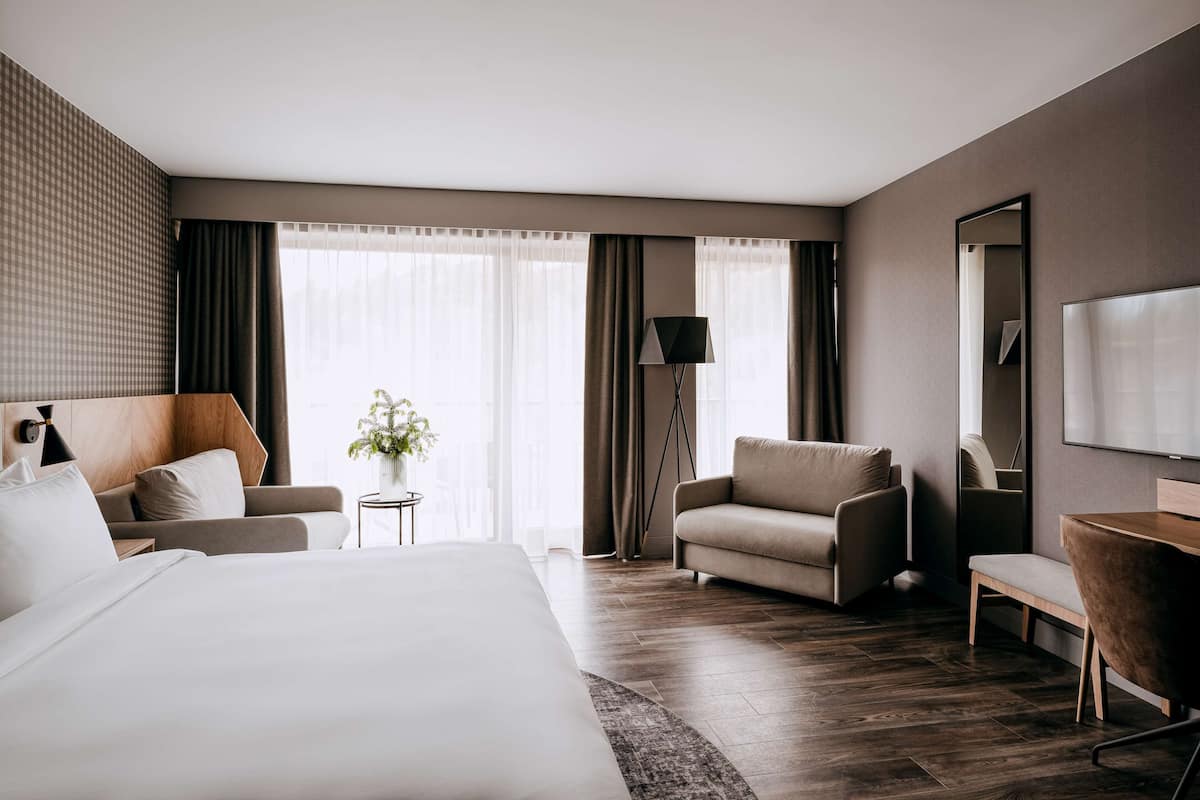 A modern hotel room with a large bed, a sofa, a desk, and a mirror.