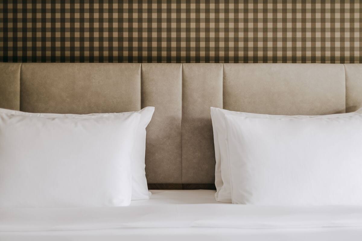 A bed with white bedding and pillows, a tufted headboard, and a checkered wall pattern.