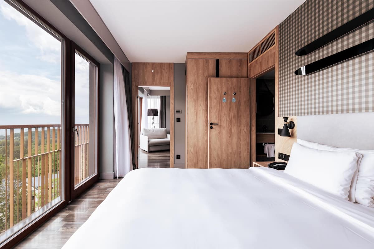 A modern hotel room with a large bed, wooden wardrobe, and a balcony with a view.