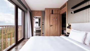 A modern hotel room with a large bed, wooden wardrobe, and a balcony with a view.