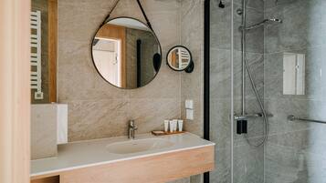 Un baño moderno con tocador de madera, espejo redondo y cabina de ducha con mampara de vidrio.