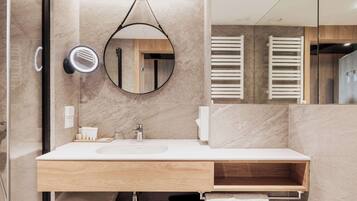 A modern bathroom with a large mirror, a round hanging mirror, a sink, and a wooden vanity.