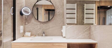 Un baño moderno con un espejo grande, un espejo redondo colgante, un lavabo y un mueble de tocador de madera.
