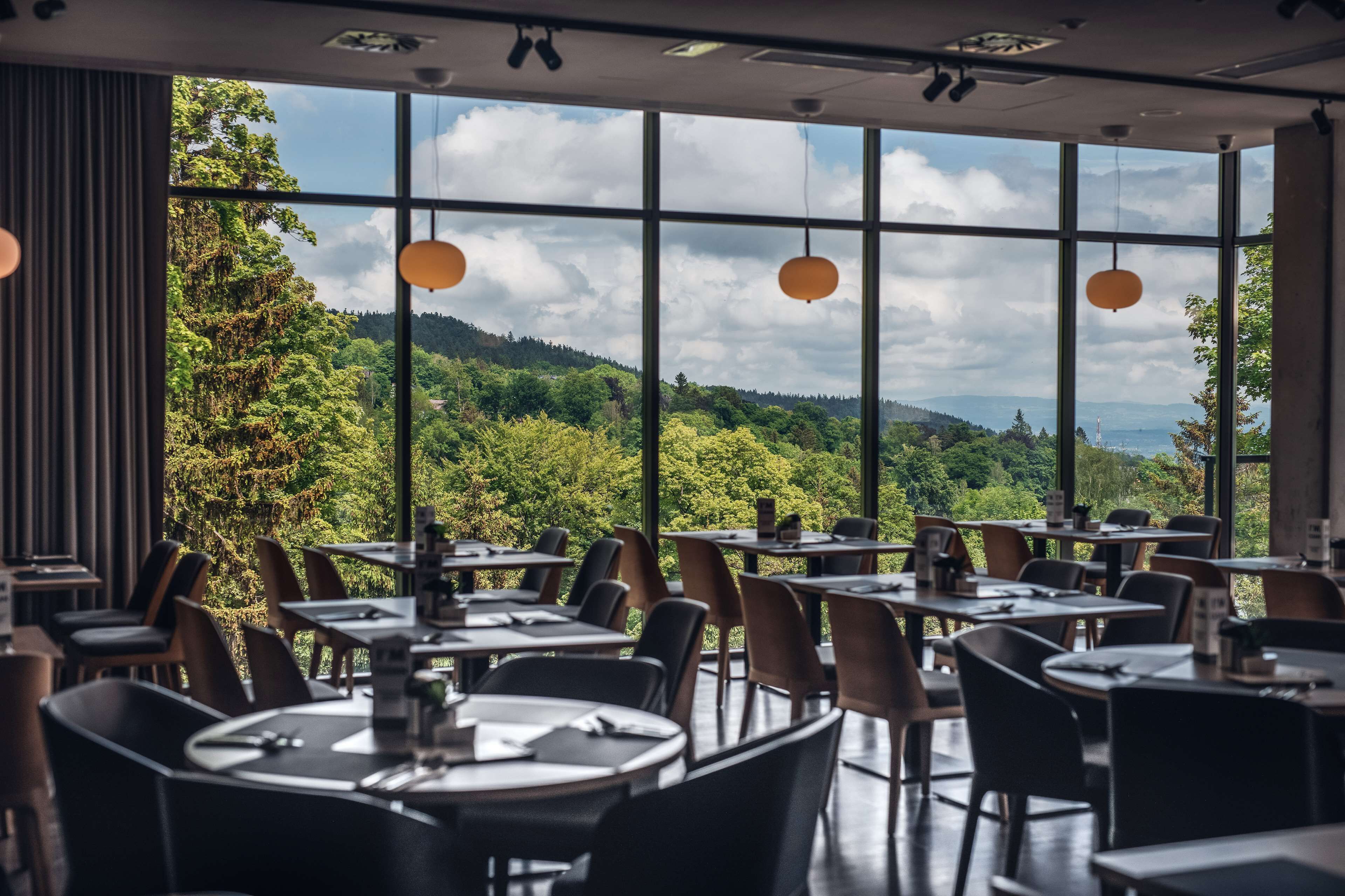 A restaurant with tables and chairs arranged for dining, large windows offering a view of a forested landscape.
