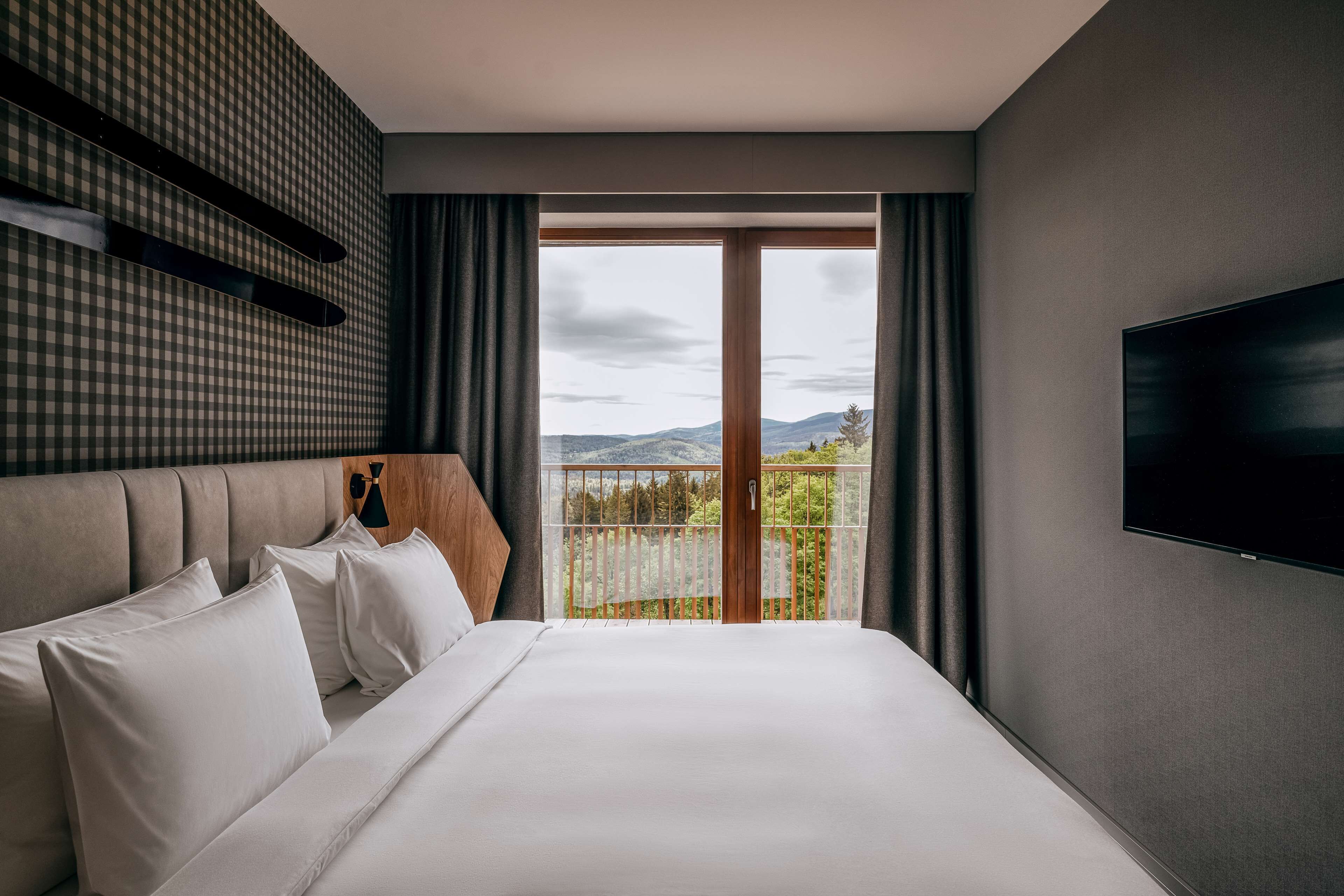 Une chambre d’hôtel moderne dotée d’un grand lit, d’une télévision à écran plat et d’un balcon offrant une vue sur les montagnes.
