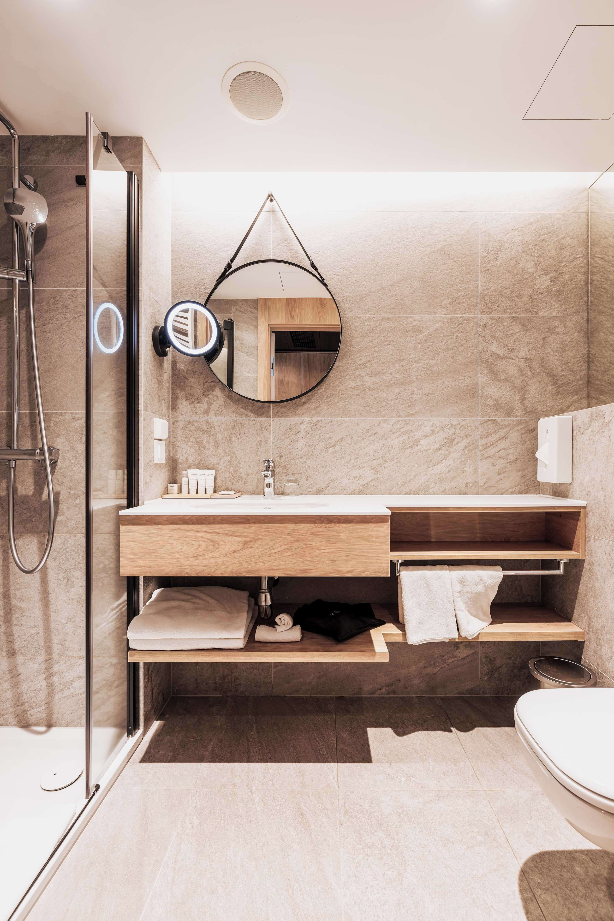 Un baño moderno con cabina de ducha de vidrio, tocador de madera con espejo y un inodoro.