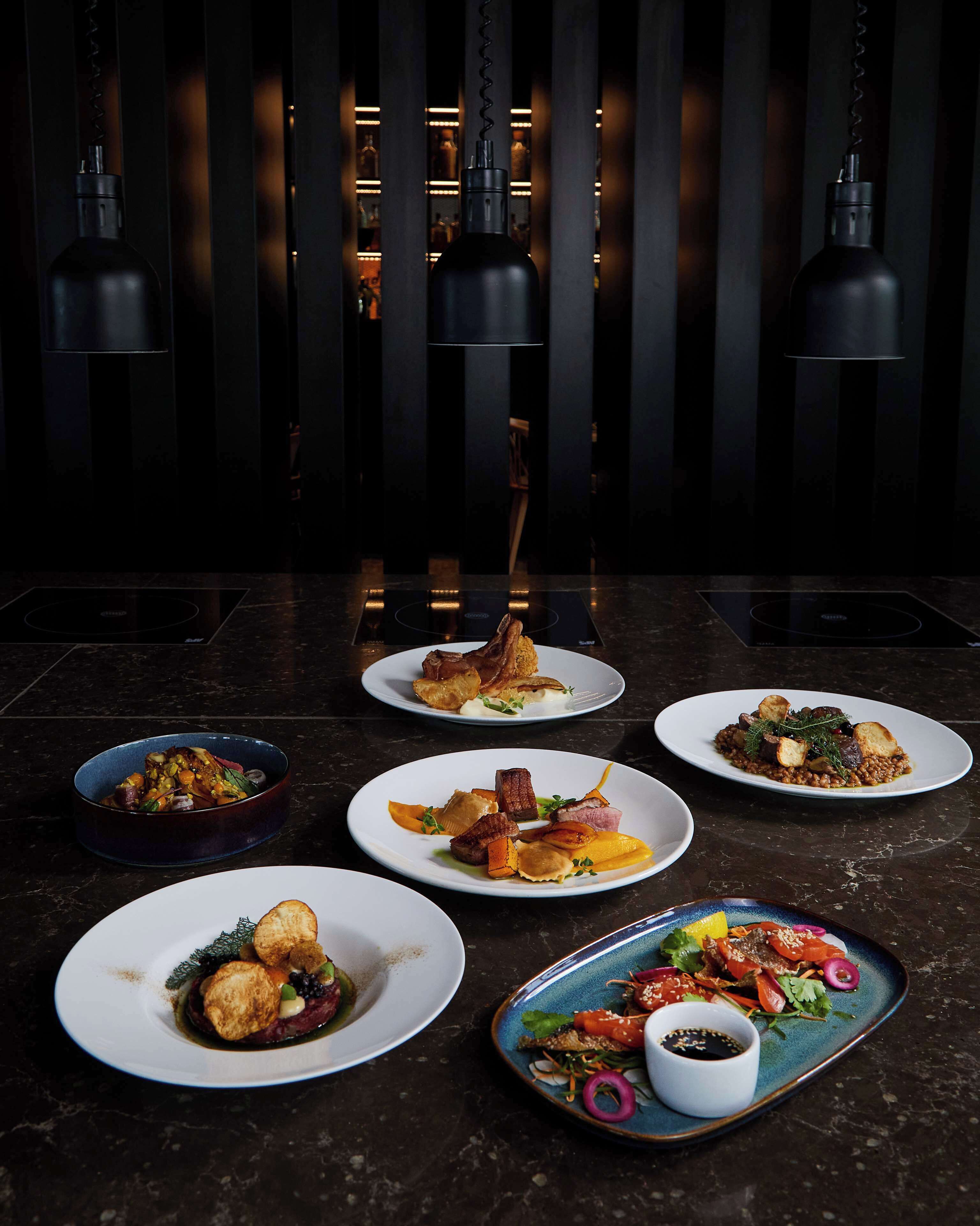 A dining area with multiple plates of food, a black countertop, and hanging pendant lights.