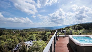 Una terraza de madera con un jacuzzi con vistas a un paisaje montañoso.