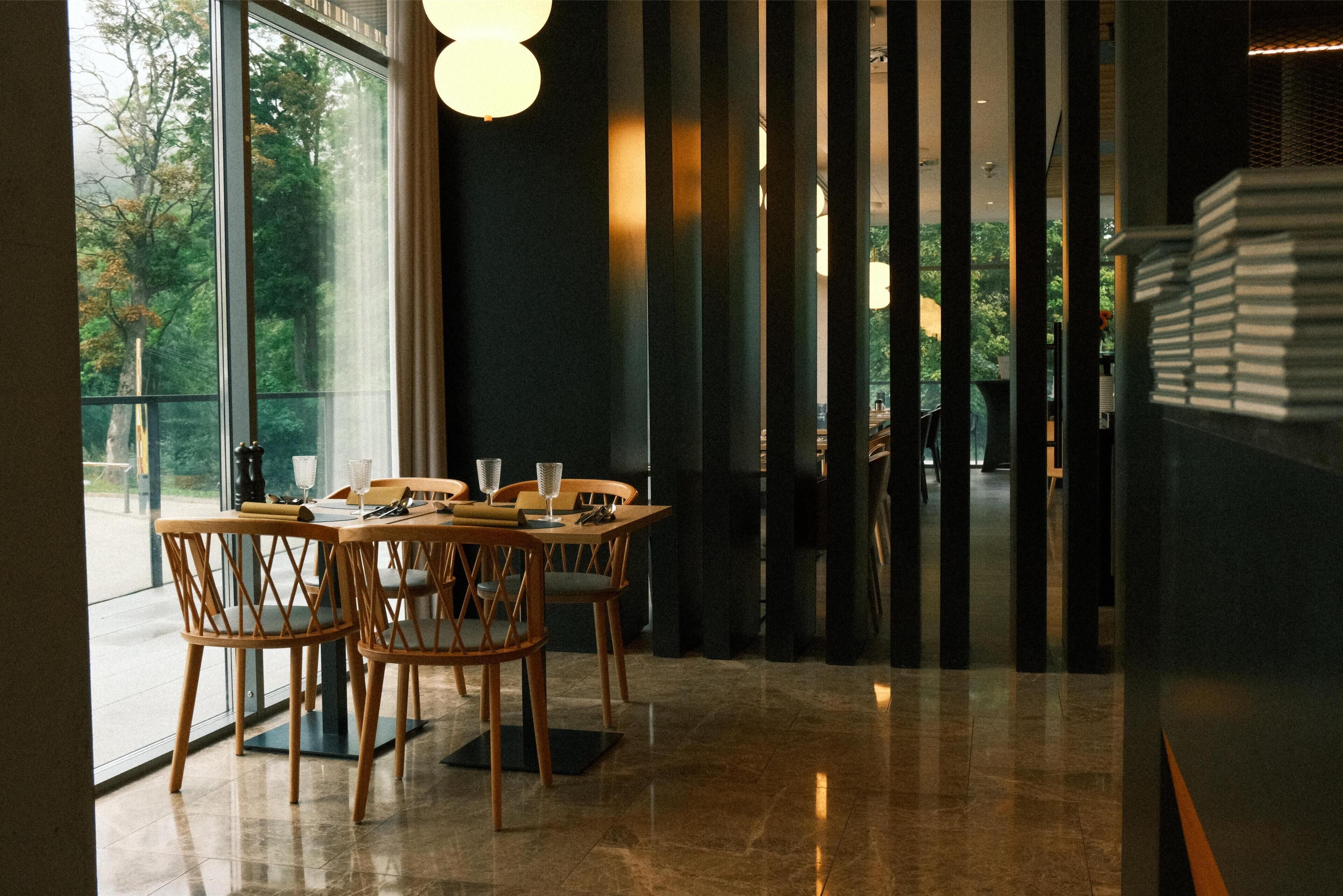 Un comedor con una mesa lista para dos personas, sillas de madera y vistas a través de amplios ventanales.