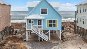 Ein Strandhaus mit zwei Etagen, einem Balkon und einer Treppe, die zum Eingang führt.