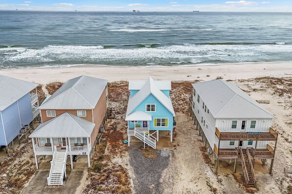 Una propiedad frente a la playa con varias casas, incluyendo una casa azul destacada con balcón y una casa blanca con terraza de madera.