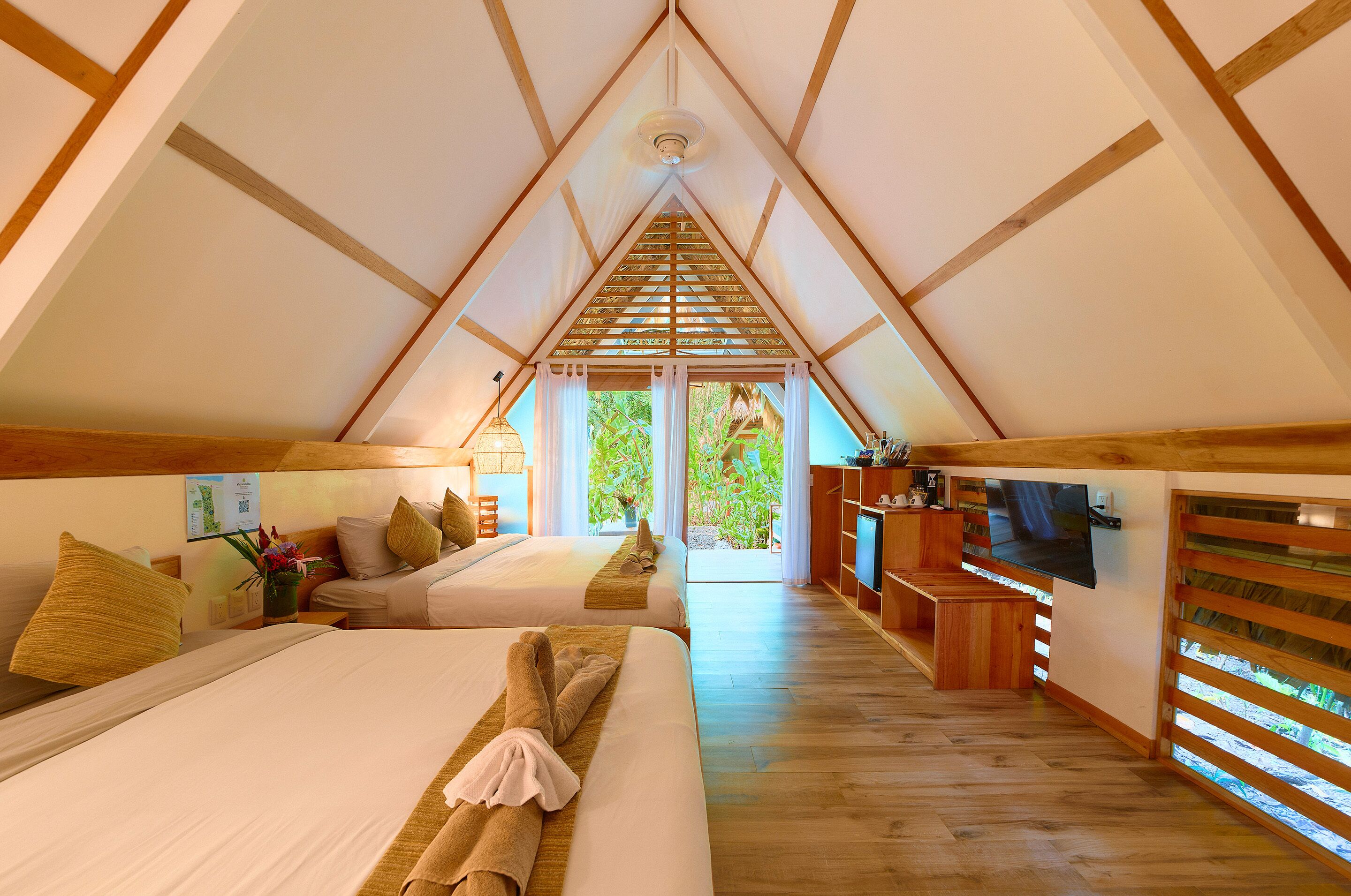 A cozy, triangular-roofed room with two beds, a TV, and a wooden desk.