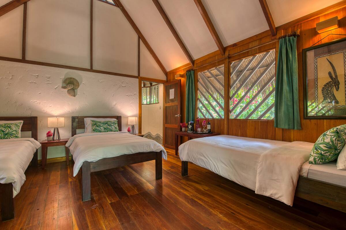 Une pièce avec un plancher en bois, deux lits, une table de chevet, une lampe et une fenêtre donnant sur un paysage verdoyant.