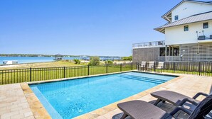 En swimmingpool med solstolar, utsikt över havet och en byggnad med en balkong.