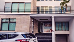 Um edifício de vários andares com design arquitetônico moderno, apresentando grandes janelas e uma entrada visível com escadaria que leva ao andar térreo.