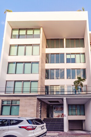 Um edifício de vários andares com design arquitetônico moderno, apresentando grandes janelas e uma entrada visível com escadaria que leva ao andar térreo.