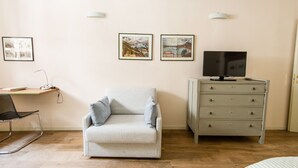 A room with a light-colored sofa, a wooden desk with a chair, a television on a cabinet, and two framed pictures on the wall. - Casa Agli Scrimiari ItalianFlat (Verona)