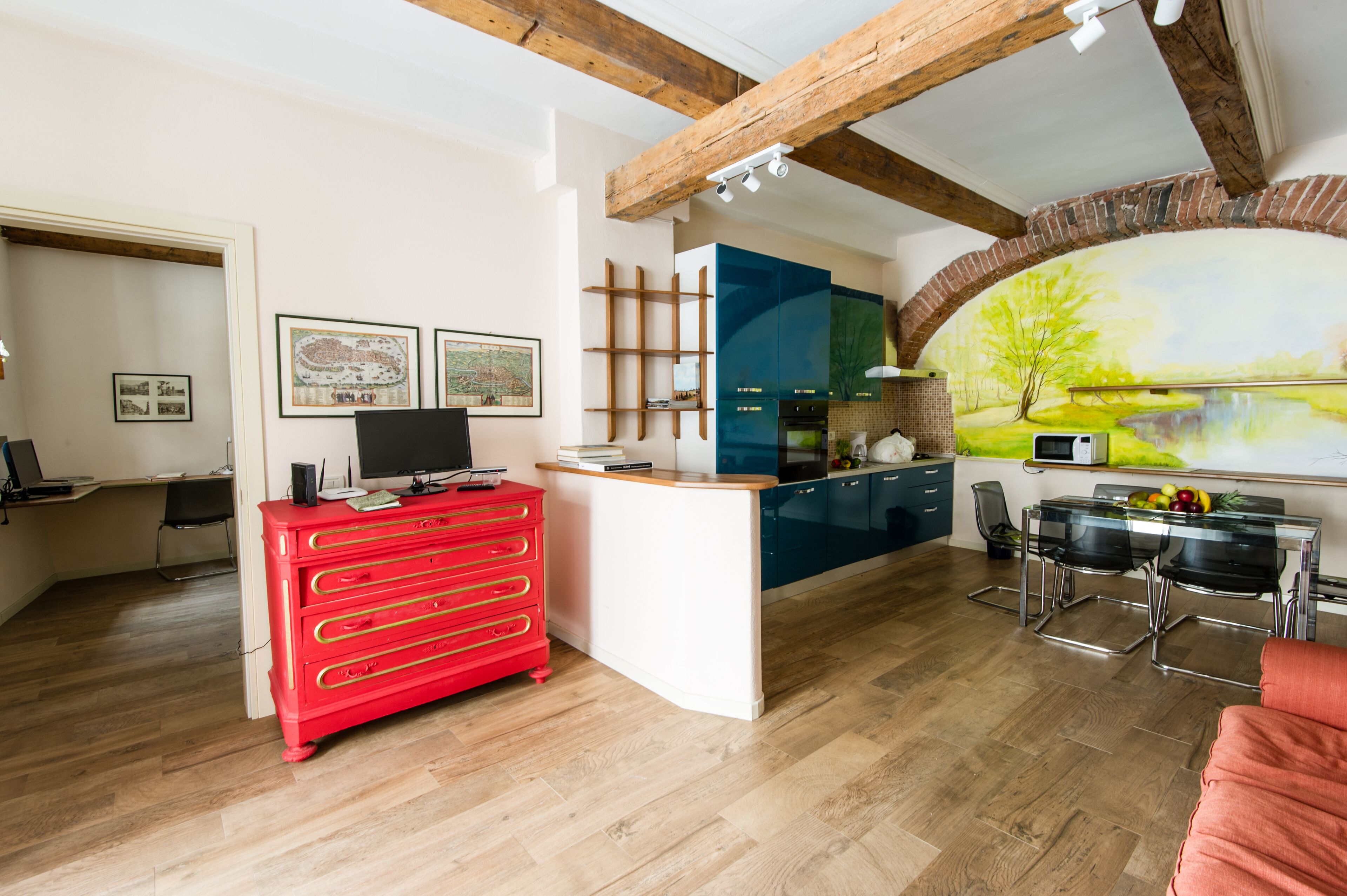 A modern kitchen with a red appliance, a dining area with a glass table, and a mural on the wall.