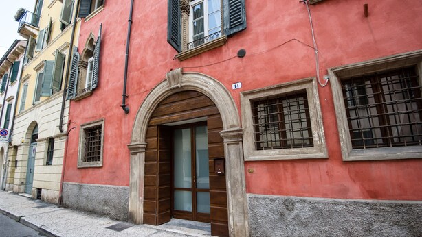 A red building with a wooden door and a balcony. - Casa Agli Scrimiari ItalianFlat (Verona)