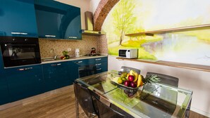 A modern kitchen with blue cabinets, a glass dining table, and a mural of a landscape. - Casa Agli Scrimiari ItalianFlat (Verona)