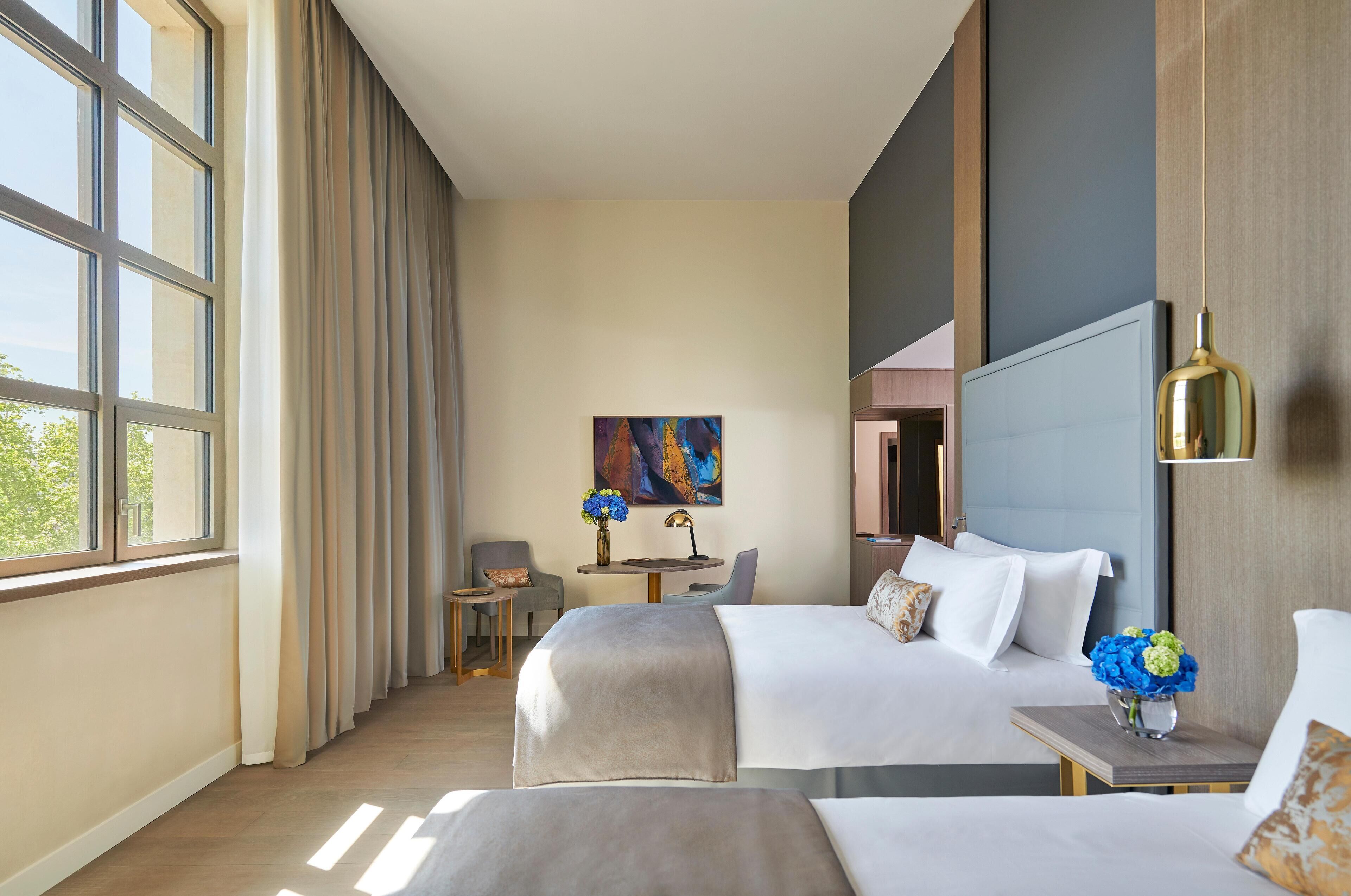A hotel room with two beds, a desk, a chair, and a painting on the wall.