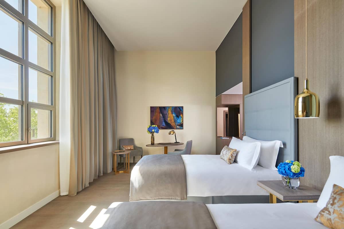 A hotel room with two beds, a desk, a chair, and a painting on the wall.