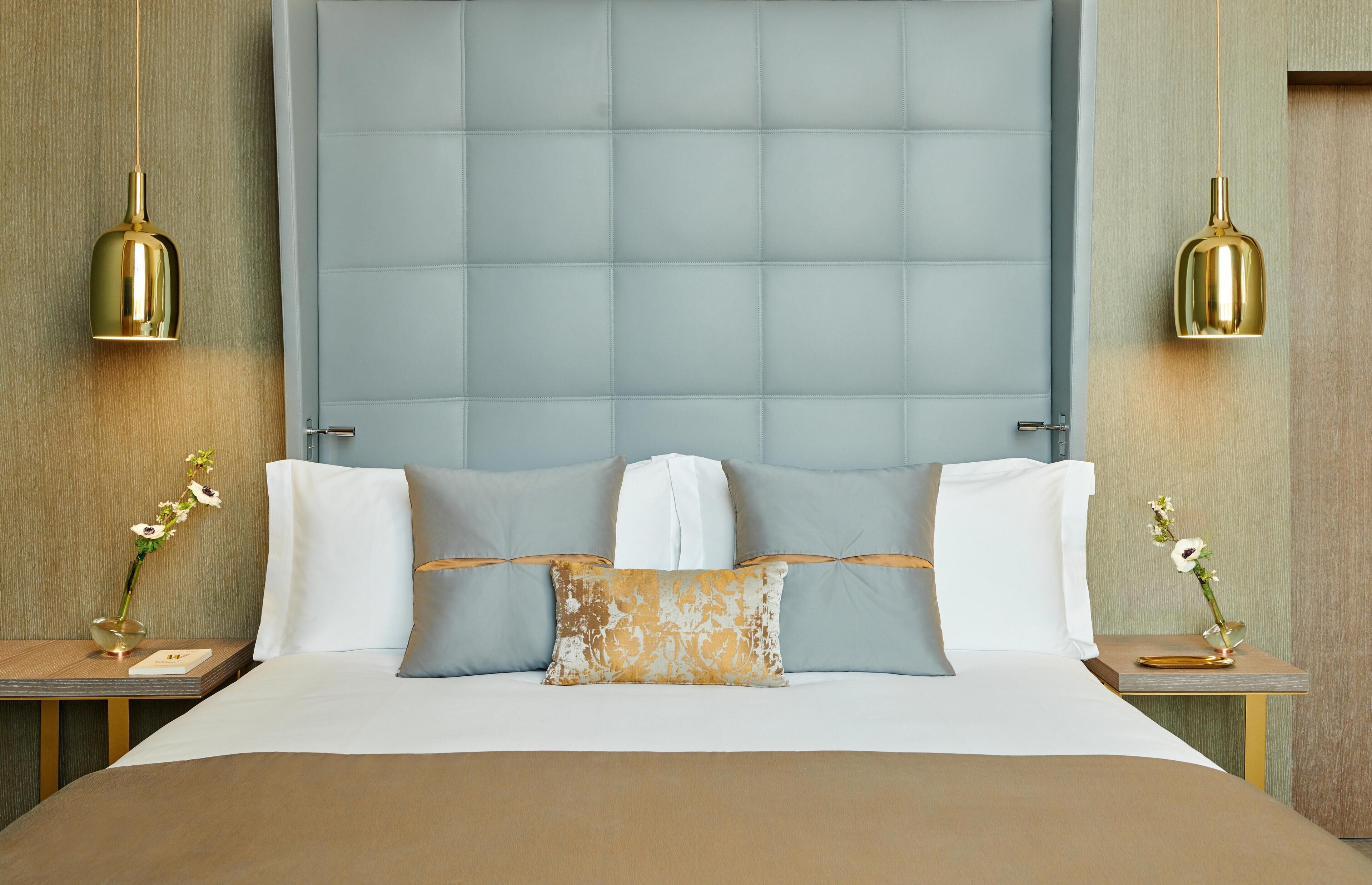 A neatly made bed with a large headboard, two bedside tables with lamps, and a vase of flowers on each side.