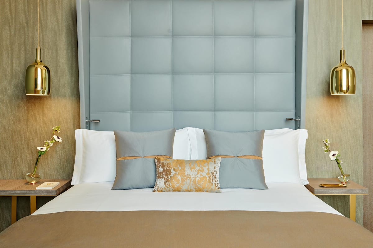 A neatly made bed with a large headboard, two bedside tables with lamps, and a vase of flowers on each side.