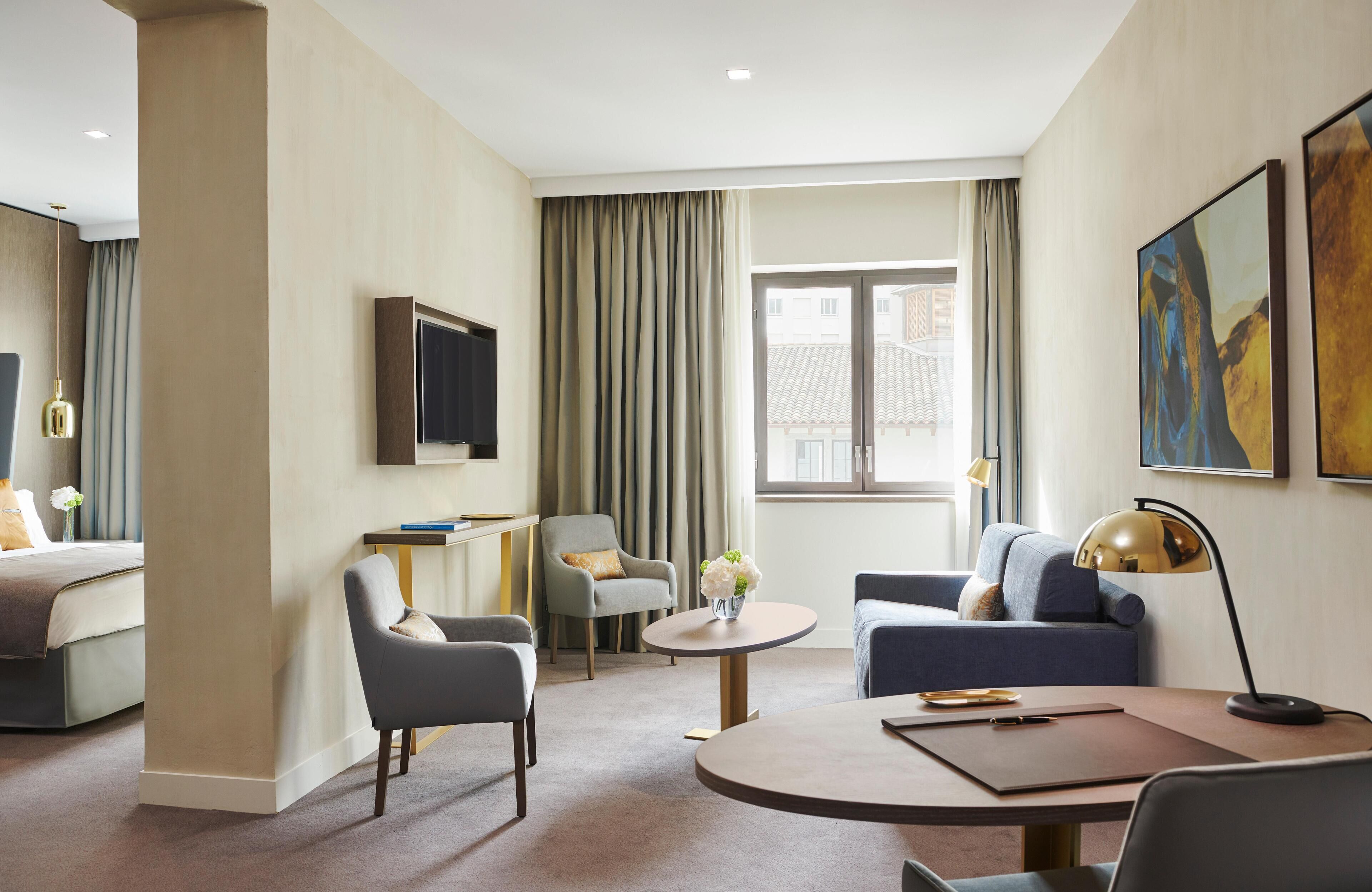 A hotel room with a bed, two armchairs, a sofa, a small table, and a TV.