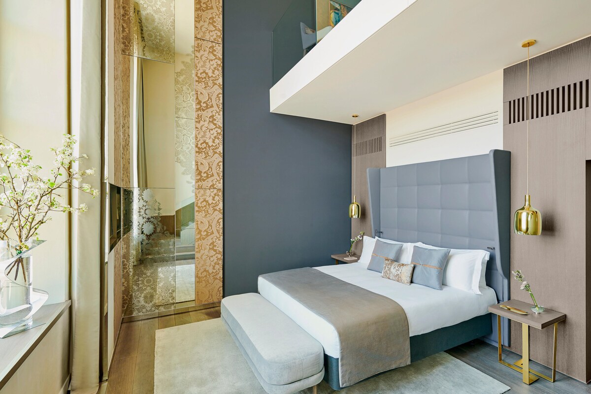 Un dormitorio moderno con una cama grande, mesitas de noche, un banco y vistas al baño.