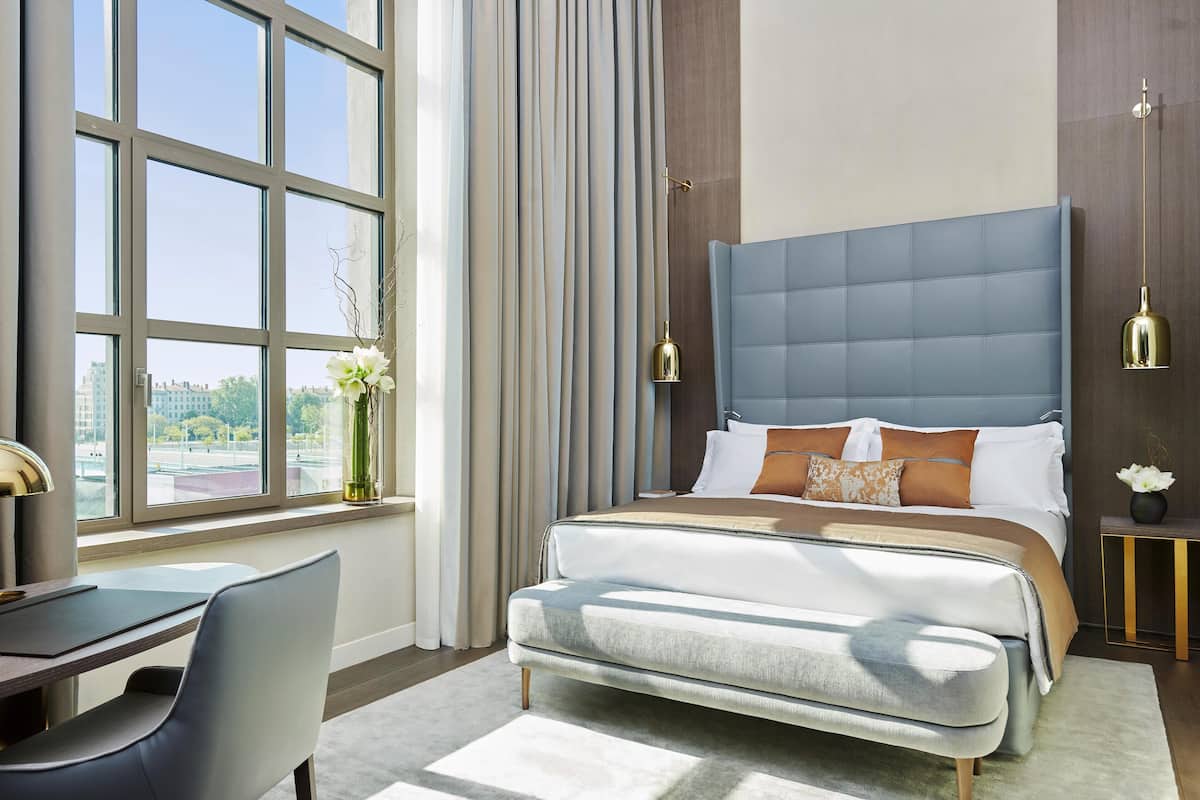 A modern hotel room with a large bed, a desk, and a view of the city.