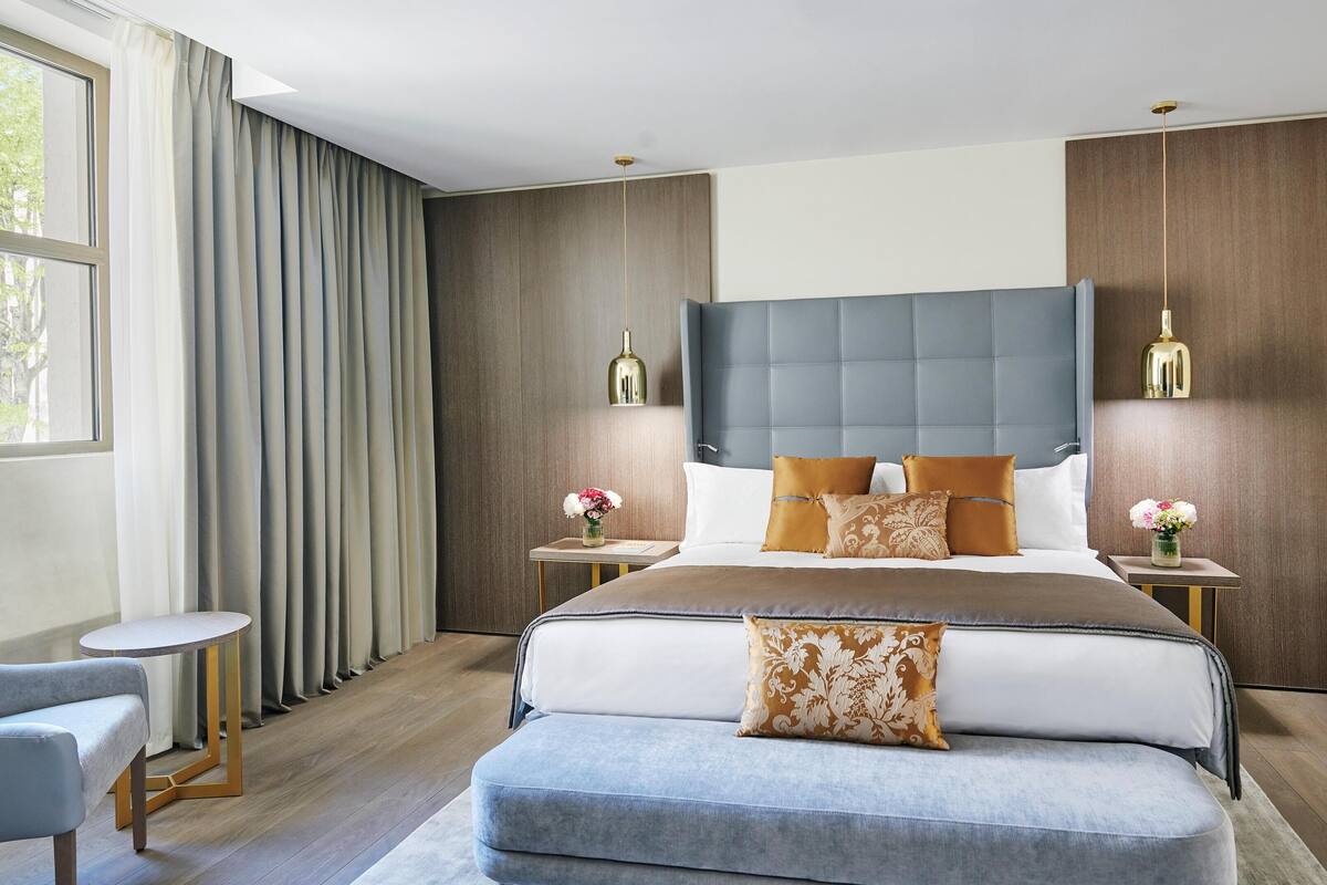 A modern bedroom with a large bed, two bedside tables, a small round table, and a bench.